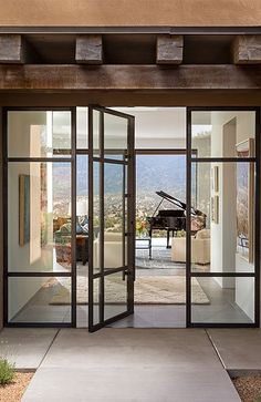 an open door leading to a living room with a grand piano in the doorway and mountains in the background