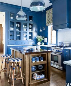 a kitchen with blue walls and wooden flooring, two stools in front of the island