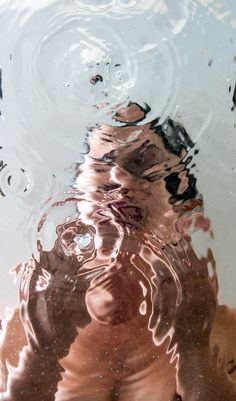 a person's reflection in the water with their hand under them and his face obscured by the water