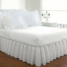 a white bed with ruffled bedspread and pillows