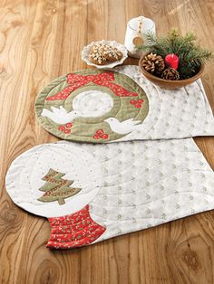 two quilted placemats sitting on top of a wooden floor next to a potted plant