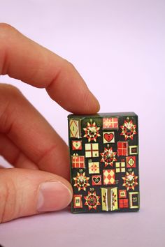 a hand is holding a small black and red square brooch with geometric designs on it