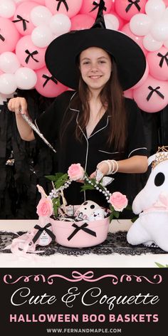 a woman in a witches hat is holding scissors and standing behind a table with pink balloons