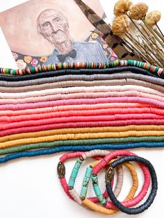 a bunch of bracelets sitting on top of a table next to a painting and flowers