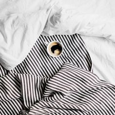 an unmade bed with black and white striped sheets, coffee cup on the pillow