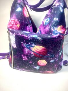 Krystal convertible shoulder bag purse, that transforms into a backpack by simply tugging the straps. Roomy medium size purse is perfect for everyday. Exterior features a galaxy outer space print on one side and coordinating purple imitation leather on the other. The outer space panel includes a slip pocket and a vertical zipper. Interior features a divided slip pocket and a zipper pocket for plenty of storage and organization. Lining is waterproof canvas. Purse is approximately 11.5" tall X 8.5 Purple Large Capacity Backpack Shoulder Bag, Purple Shoulder Backpack For Daily Use, Purple Satchel Backpack For Daily Use, Trendy Purple Shoulder Backpack, Versatile Purple Shoulder Bag With Zipper, Purple Backpack With Zipper Closure, Versatile Purple Bag With Adjustable Strap, Purple Backpack Shoulder Bag For Everyday Use, Purple Satchel Backpack With Adjustable Strap