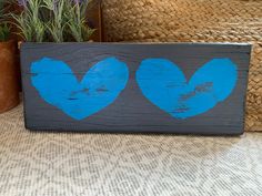 two blue hearts are painted on a gray wood block with some plants in the background