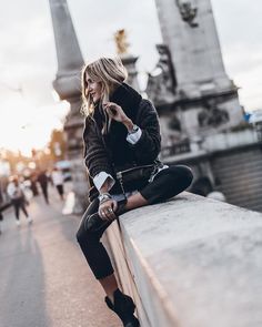 a woman sitting on the edge of a bridge looking at her cell phone while wearing black and white