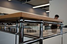 a person sitting at a table in an office setting with stainless steel railings and wood top