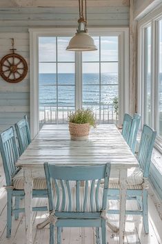 a dining room table with blue chairs and an ocean view out the window in front of it