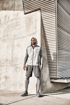 a man standing in front of a building wearing a hoodie and sweatpants with his hands on his hips