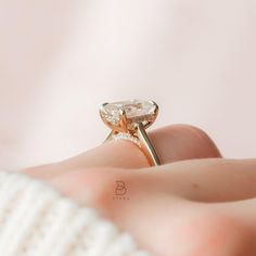 a woman's hand holding a ring with an oval shaped diamond on it, in front of a pink background