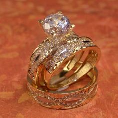 three gold wedding rings with diamond accents on a red cloth covered tablecloth in front of an orange background