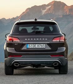 the rear end of a black suv parked in front of mountains