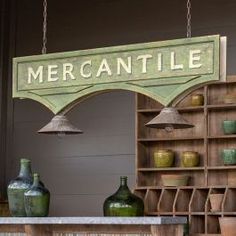 a sign that says mercantile hanging from the side of a wall next to vases