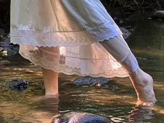 a woman in white dress standing on top of a rock next to a body of water