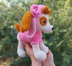 a crocheted dog with a pink scarf on it's head is being held by a hand