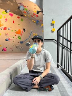 a young man sitting on the ground drinking from a water bottle while wearing a hat