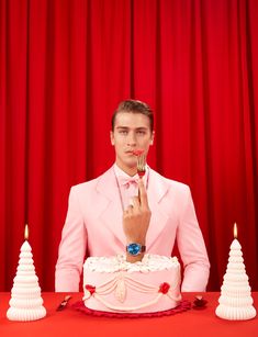 a man in a pink suit holding a fork up to his mouth while standing next to a cake