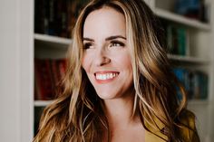 a woman with long hair smiling in front of a bookshelf and bookcase