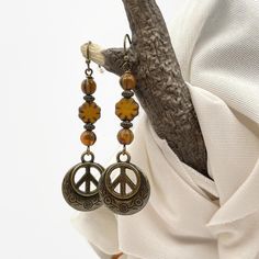 Add a touch of bohemian charm to your outfit with these burnt orange and bronze peace sign dangle drop earrings. The handcrafted earrings feature a bronze, 20mm peace sign charm, and the total length of the earrings measures 2-3/8 inches. The main beads are Czech glass with a beautiful burnt orange color. These earrings are perfect for anyone looking to add a unique and stylish touch to their jewelry collection. They are nickel-free and feature a boho chic theme that is perfect for any occasion. Boho Earrings Hippie Bohemian, Flower Bead Earrings, Jewelry 70s, Peace Sign Jewelry, Hippie Styles, Peace Sign Earrings, Peace Earrings, Style Festival, Glass Bead Earrings