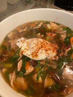 a bowl of soup with meat, vegetables and an egg in it on a table