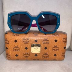 Brand New. Authentic Mcm Dual (Blue And Purple) Sunglasses. Frame Is Squared Butterfly Shape With Gold Studs To Outline. The Mcm Brand Logo On Each Temple. Lens Is Like Smoke Color. I Love The Flair And Mixture Of Colors On These Sunglasses. Very Classy And Compliments The Wardrobe. Size: Adult - 55/16/140 (Eye/Temple/Bridge). Comes With The Mcm Case And Cleaning Cloth Formal Purple Sunglasses With Tinted Lenses, Formal Purple Tinted Sunglasses, Designer Purple Sunglasses With Gradient Lenses, Designer Blue Sunglasses With Gradient Lenses, Designer Purple Sunglasses With Tinted Lenses, Designer Purple Tinted Sunglasses, Luxury Blue Sunglasses With Uva Protection, Blue Sunglasses With Uv Protection For Formal Occasions, Luxury Purple Sunglasses For Summer