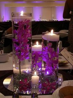 two tall glass vases with flowers and candles on a table in front of people