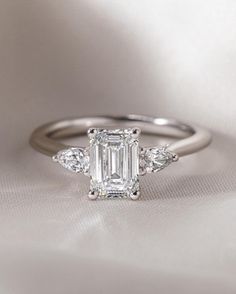 an emerald cut diamond ring with three diamonds on the band and side stones in white gold