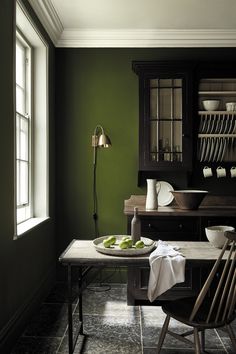 a dining room with green walls and wooden furniture in the corner, along with dishes on a table