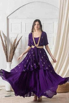 Strut around in this contemporary style indo-western dress in deep amethyst hue with contrasting golden handwork. Designed with eye-catching floral motifs and a wrapped silhouette, this dress has the required sophistication and charm. With a deep V neck and knotted appeal, style it with layered necklace and earrings for an event-ready ensemble you'll adore.Style Wrap style dress Knotted closure Ankle length style Embroidered lace detailing All over motif embroidery Decadent amethyst color George Elegant Purple Sharara For Party, Elegant Purple Kurta With Mirror Work, Front Open Georgette Wedding Dress, Wedding Georgette Dress Front Open, Front Open Georgette Dress With Zari Work, Elegant Front Open Designer Dresses, Designer Front Open Georgette Dress, Designer Georgette Dress With Front Open, Purple Embellished Floor-length Sets