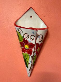 a decorative vase hanging on the wall with an orange background and red flowers painted on it