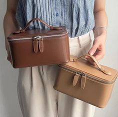 a woman holding two brown and tan suitcases in her hands, both with zippered handles