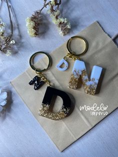 two keychains with letters on them sitting next to some dried flowers and paper