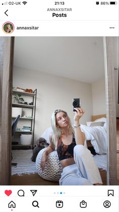 a woman taking a selfie with her phone in front of the camera, while sitting on a bed