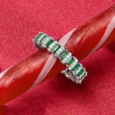 an emerald and diamond ring sitting on top of a red piece of candy canes