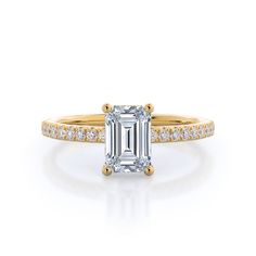 an emerald cut engagement ring with diamonds on the band and side stones in rose gold