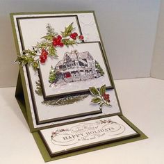 a christmas card with holly and red berries on the front, sitting on a white surface