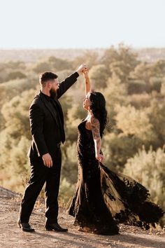 a man and woman standing on top of a dirt field next to each other with trees in the background