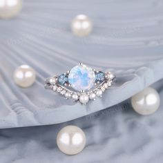 an opal and pearl ring sits on a white background with pearls scattered around it