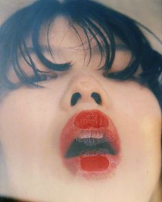 a woman's face with her mouth open and red lipstick painted on the lips