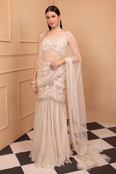 Ivory pre-stitched lehenga saree with intricate embroidery in gold and ivory shades of sequins, pearls and glass beads work. Paired with embroidered blouse with floral motifs.
Components: 2
Pattern: Embroidery
Type Of Work: Sequin, Pearl, Glass Bead, Floral
Neckline: Sweetheart neck
Sleeve Type: Sleeveless
Fabric: Net
Color: Ivory
Other Details: 
Fischcut style lehenga saree
Ruffle on pallu hem
Pearl tassel detailing on shoulder strap
Back tassel tie-up
Inverted V hem
Model height: 5ft 8inches, Elegant White Pre-draped Saree For Eid, Elegant Off-white Lehenga For Festive Occasions, Festive Semi-stitched Cream Pre-draped Saree, Elegant Off White Dupatta For Reception, Elegant Off-white Dupatta For Reception, Elegant Pre-draped Saree For Wedding And Eid, Cream Lehenga With Traditional Drape For Parties, Cream Semi-stitched Gown With Pallu, Semi-stitched Cream Lehenga For Party