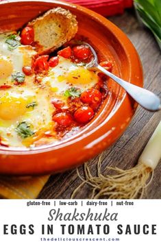 an orange bowl filled with eggs and tomatoes on top of a table next to bread