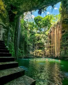 some people are swimming in the water near rocks and trees, while another person is standing on stairs above them