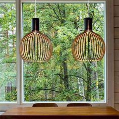 two lamps hanging over a wooden table in front of a large window with trees outside