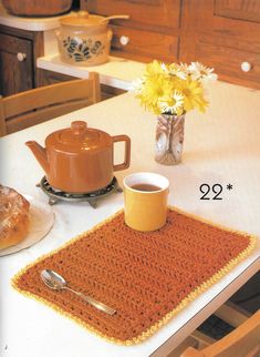 a crocheted placemat on a table with a tea pot and coffee cup