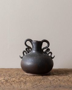 an old black vase sitting on top of a wooden table next to a white wall