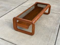 a wooden table sitting on top of a cement floor next to a sidewalk with no one around it