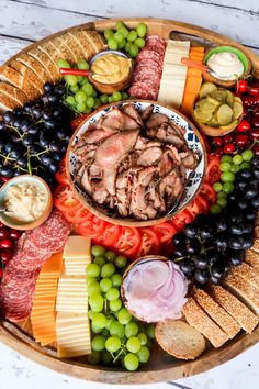 a platter filled with meat, cheeses, crackers and grapes on a table