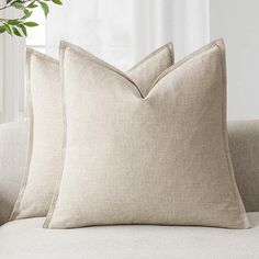 two beige pillows sitting on top of a couch next to a potted green plant